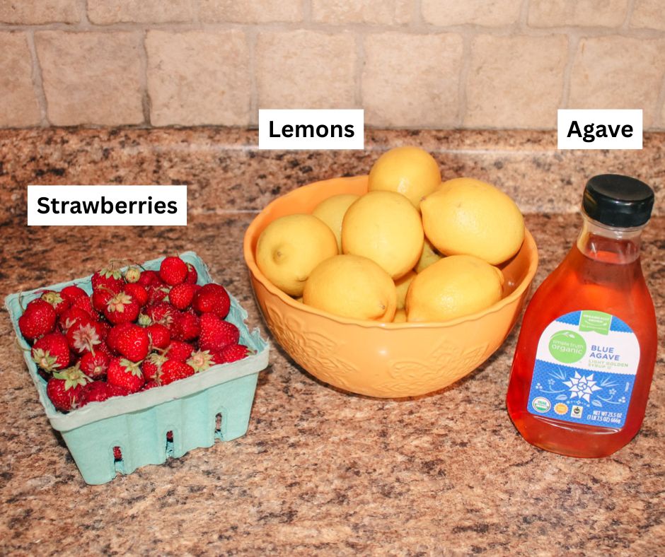 ingredients to make strawberry lemonade sit on a speckled kitchen countertop
