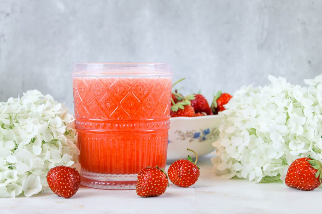 glass of sugar free strawberry lemonade surrounded by fresh berries and white flowers