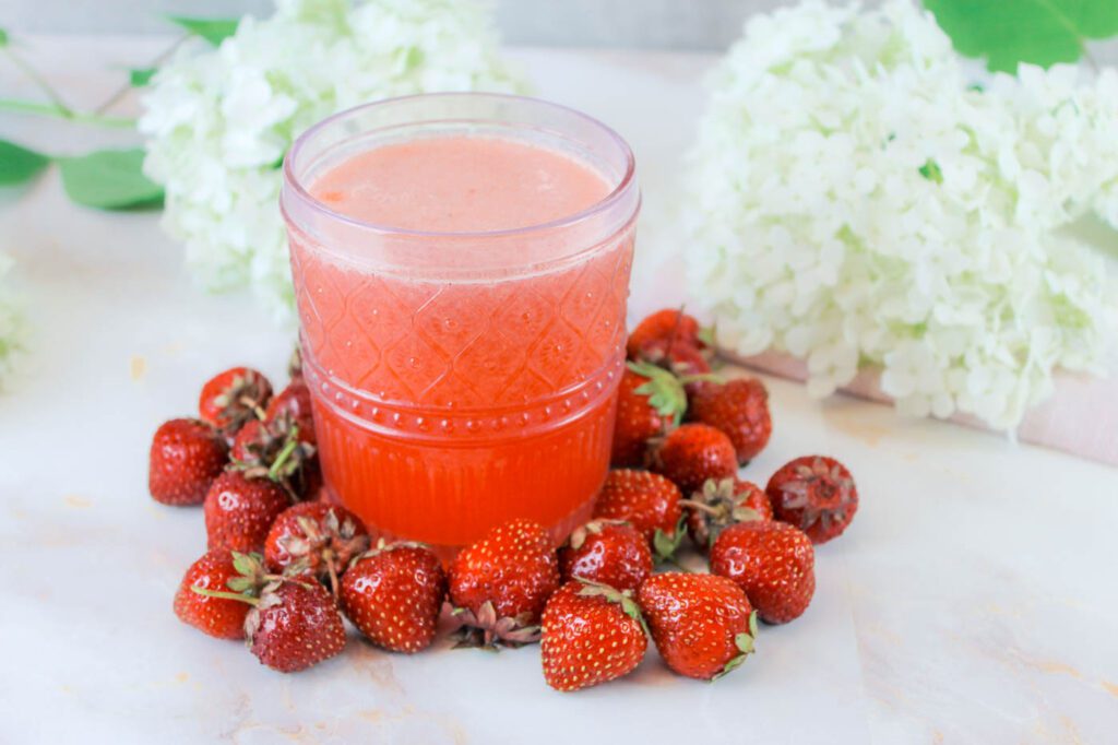 pink glass cup filled with homemade lemonade sits surrounded by a pile of fresh strawberries