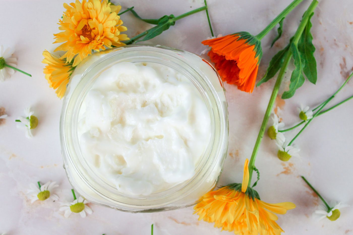 top view of a glass jar filled with whipped body butter sits besides pieces of chamomile