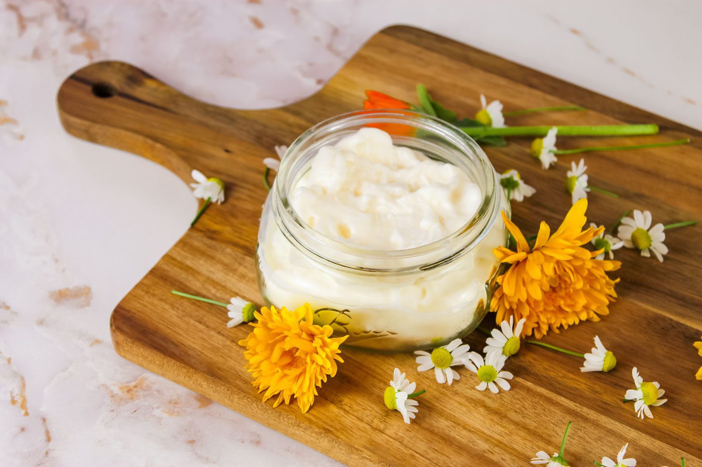 glass mason jar filled with homemade whipped body butter sits surrounded by fresh flowers