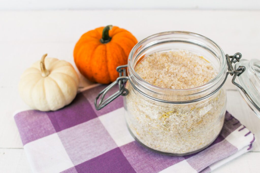 jar of fall scented bath soak beside a small white and orange pumpkin