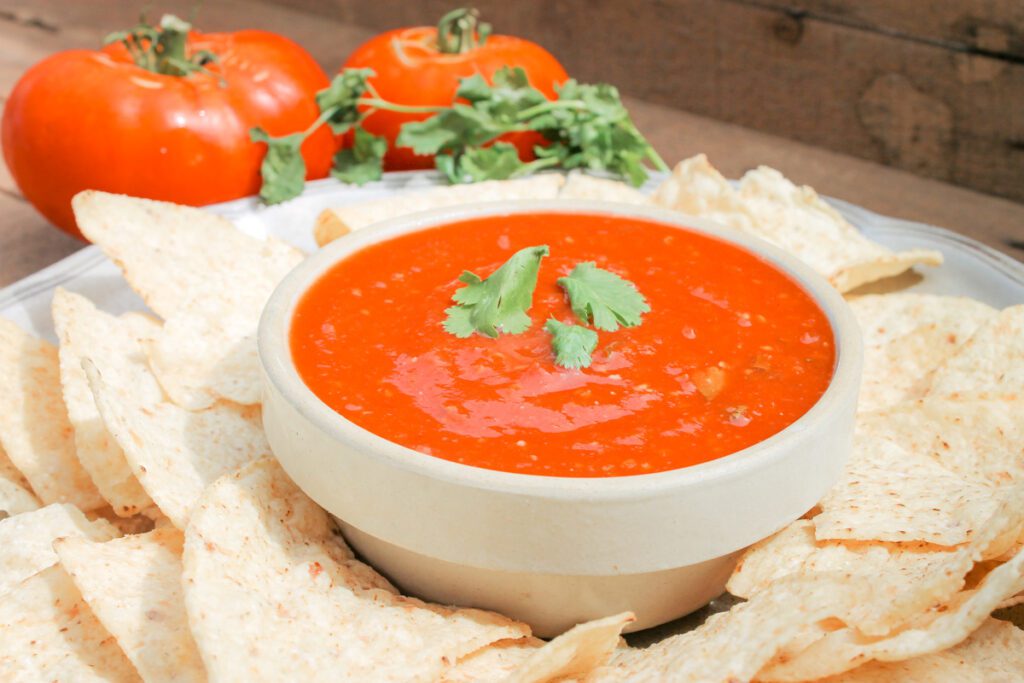 bowl of homemade salsa beside a plate of chips and 2 large tomatoes
