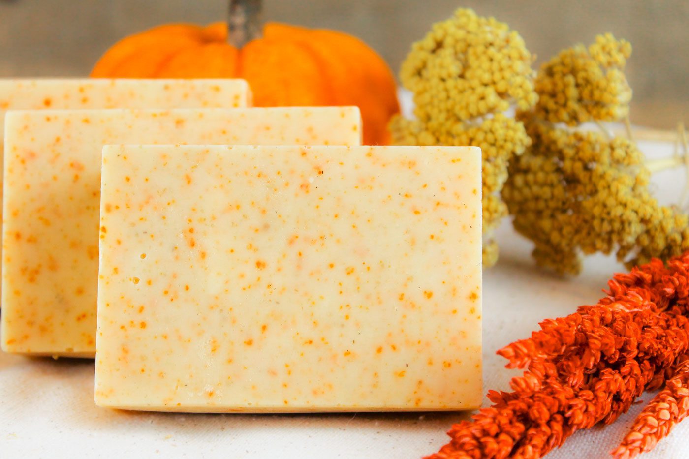 autumn spice soap bars sit beside dried fall florals and an orange pumpkin