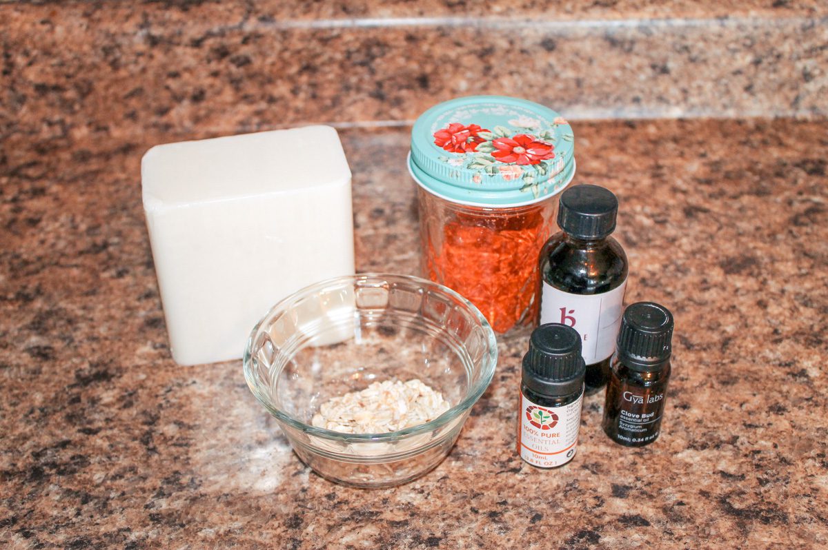 soap making ingredients including oats, a melt and pour soap base and essential oils sit on a countertop