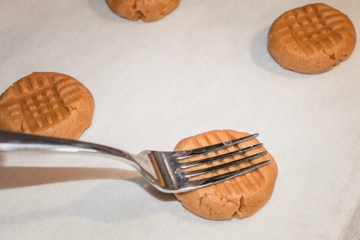 a fork presses into a peanut butter cookie to make a criss cross pattern