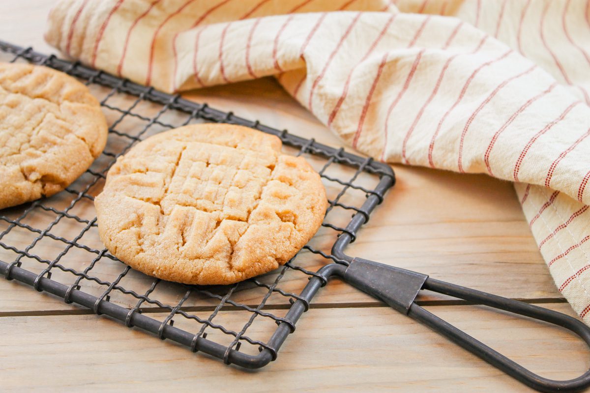 peanut butter cookie recipe displayed on a cooling rack besides a striped kitchen towel