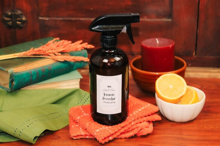 glass bottle of lemon cedar dusting spray sits on cleaning rags surrounded by home decor