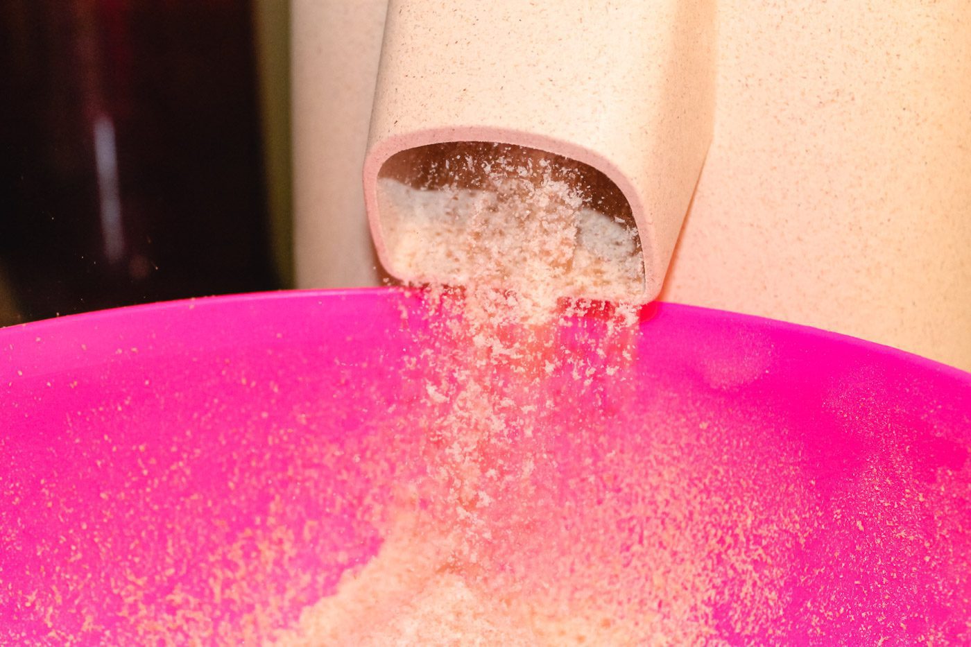 stone grain mill grinding flour into a pink bowl
