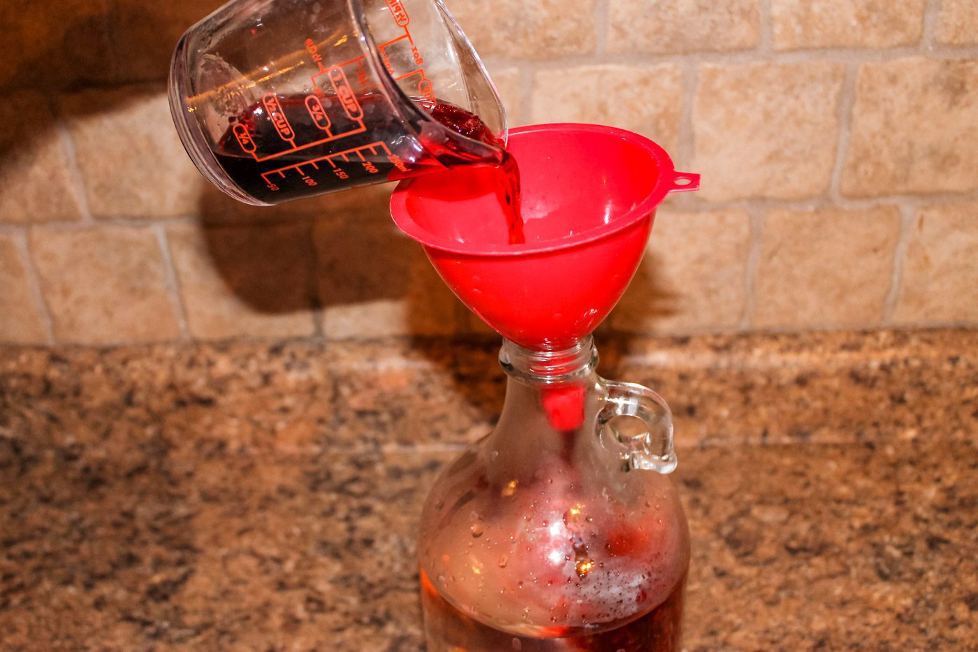 measuring cup filled with cherry juice fills a half gallon glass container