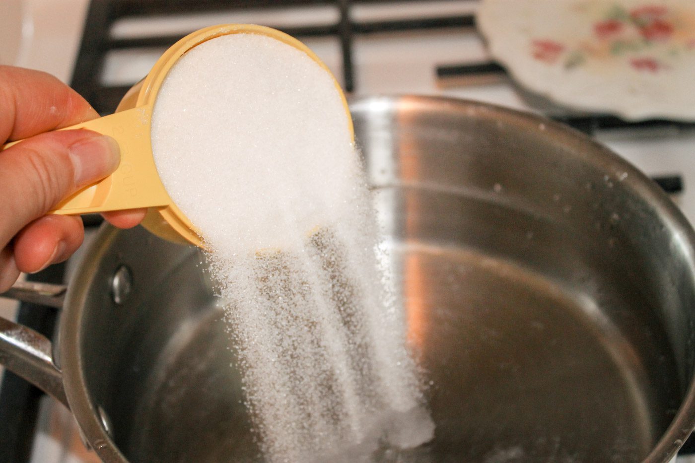 woman pours a cup of sugar into a pot of water