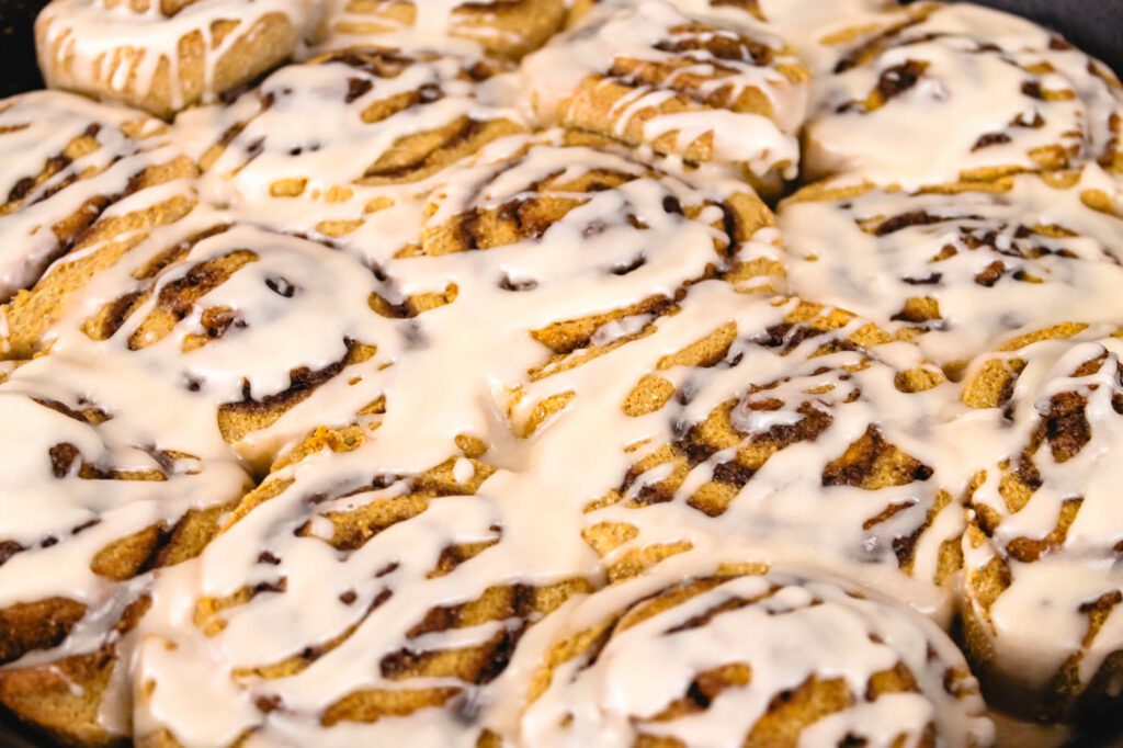 pan full of freshly baked rolls covered in frosting