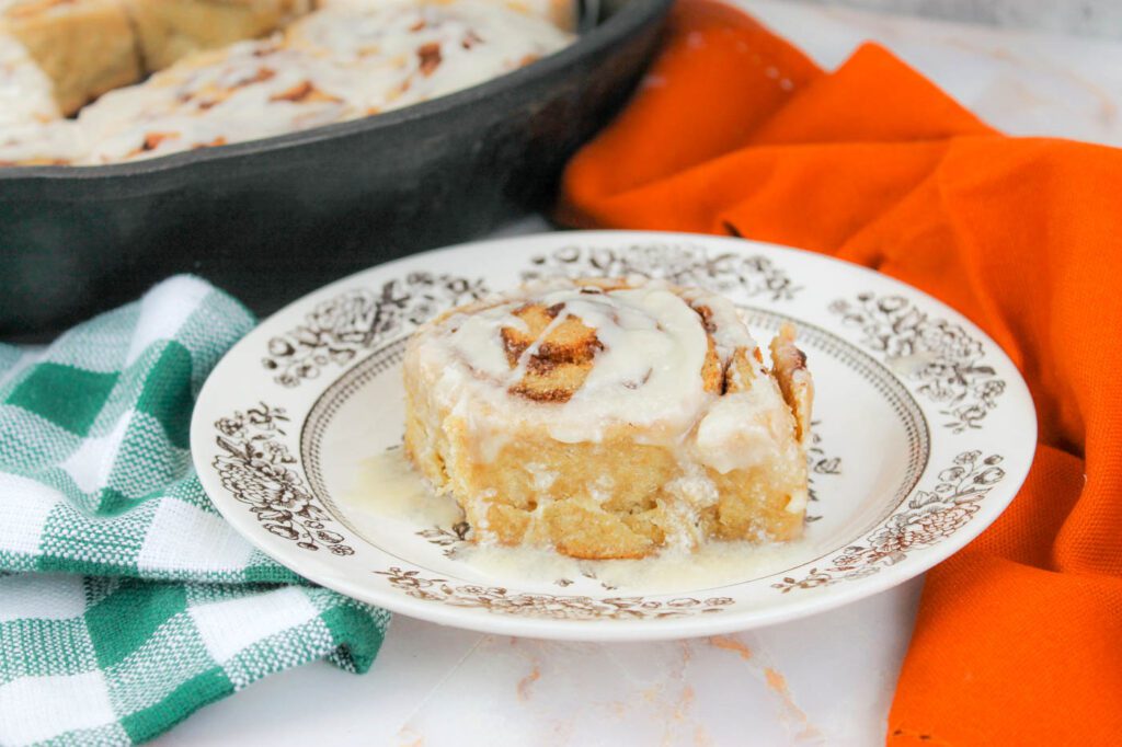 pan filled with cinnamon rolls with fresh milled flour sits behind a plate with a single roll