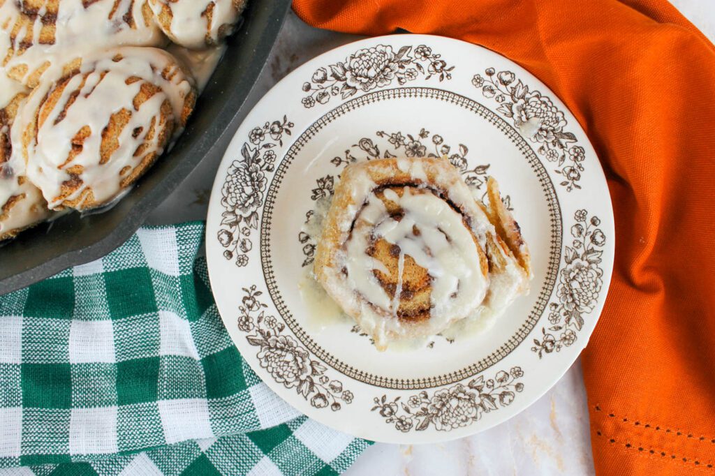 top view of a cinnamon roll on a plate surrounded by colorful kitchen towels