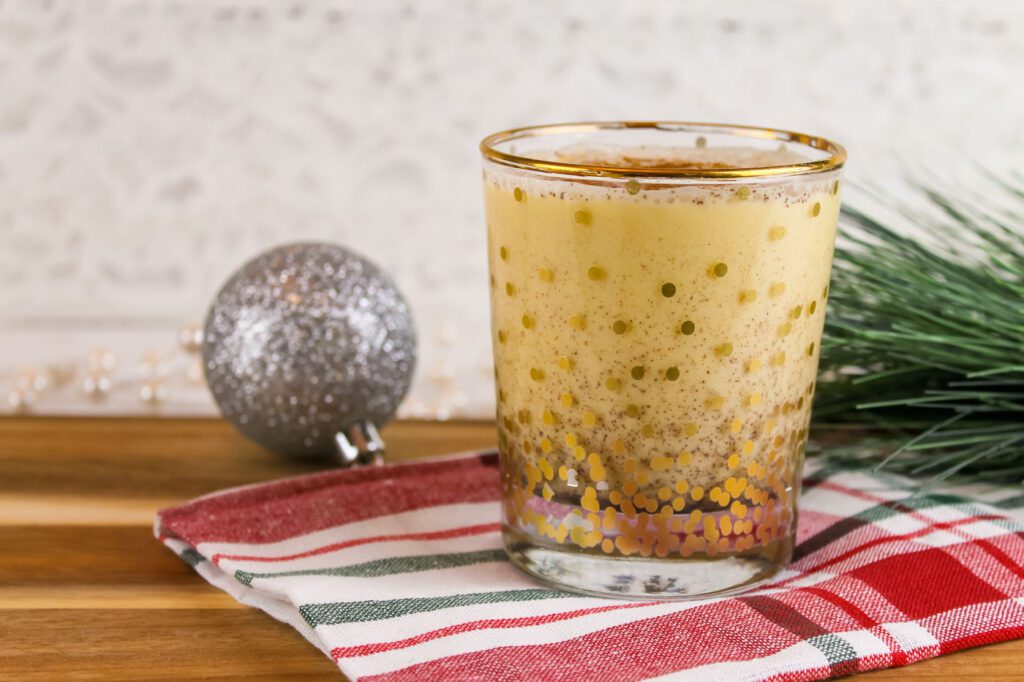 holiday cup filled with homemade eggnog sitting beside a Christmas ornament