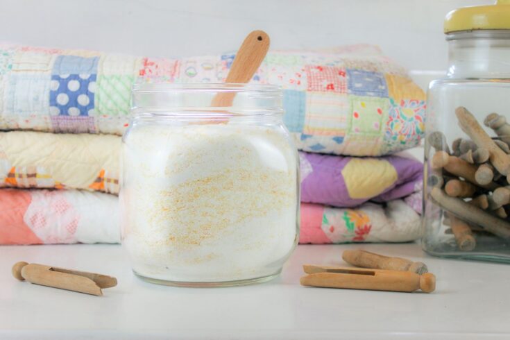 jar of powdered laundry detergent sits in front of a pile of vintage quilts