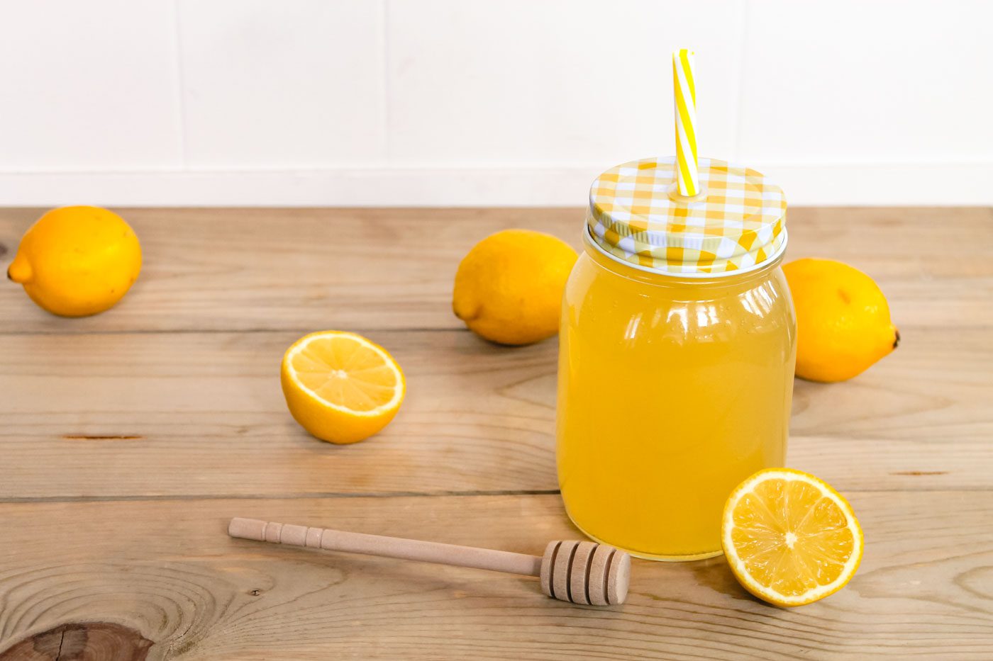 mason jar with yellow plaid lid and striped yellow straw. inside the jar is lemonade.