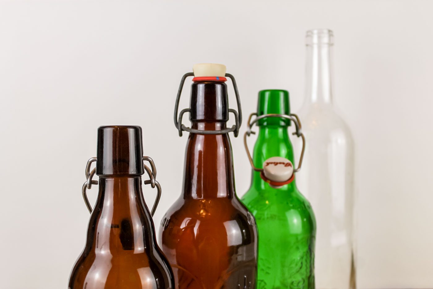4 fermentation bottles sit in a line, two are amber colored, one is green and the last one is clear glass
