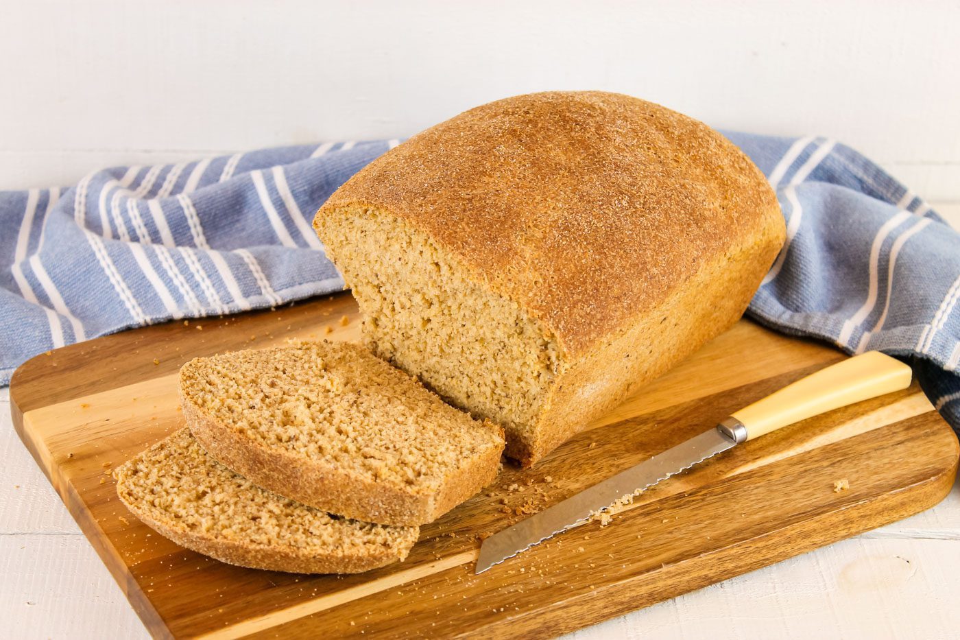loaf of bread with two slices sits next to a bread knife and blue kitchen towel