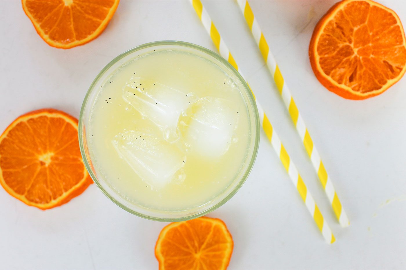 glass of orange cream soda sits next to orange slices and bright yellow straws