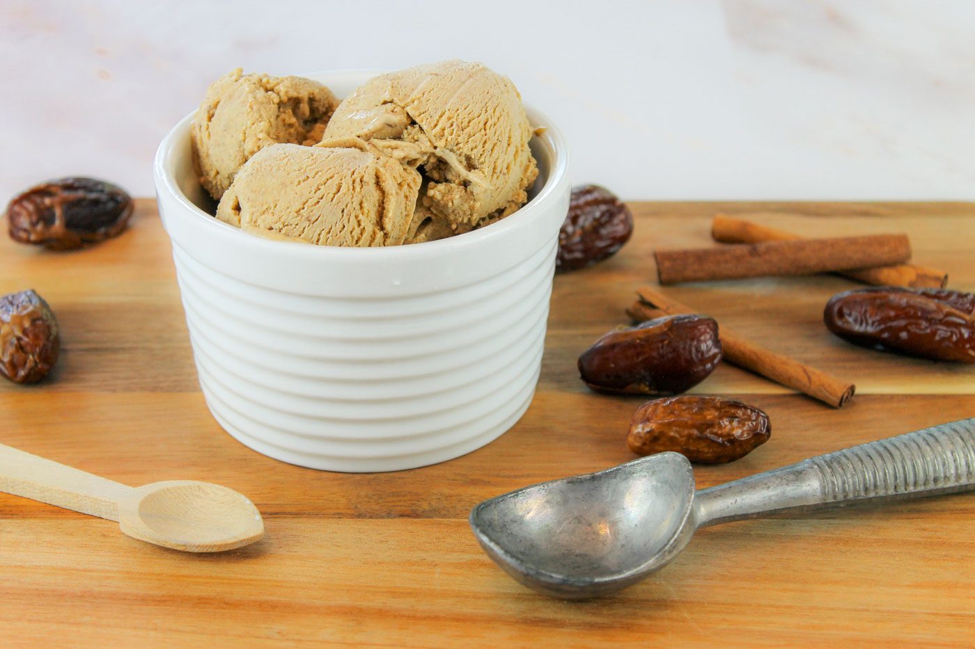 striped ceramic bowl full of ice cream sits surrounded by cinnamon sticks and dried dates