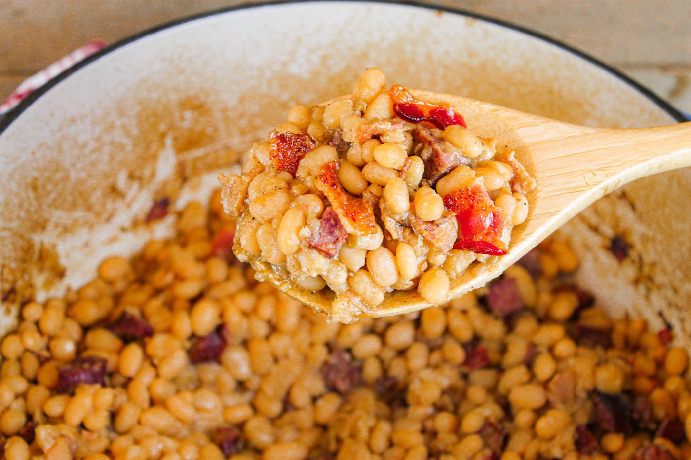 wooden spoon full of a large amount of baked beans and bacon