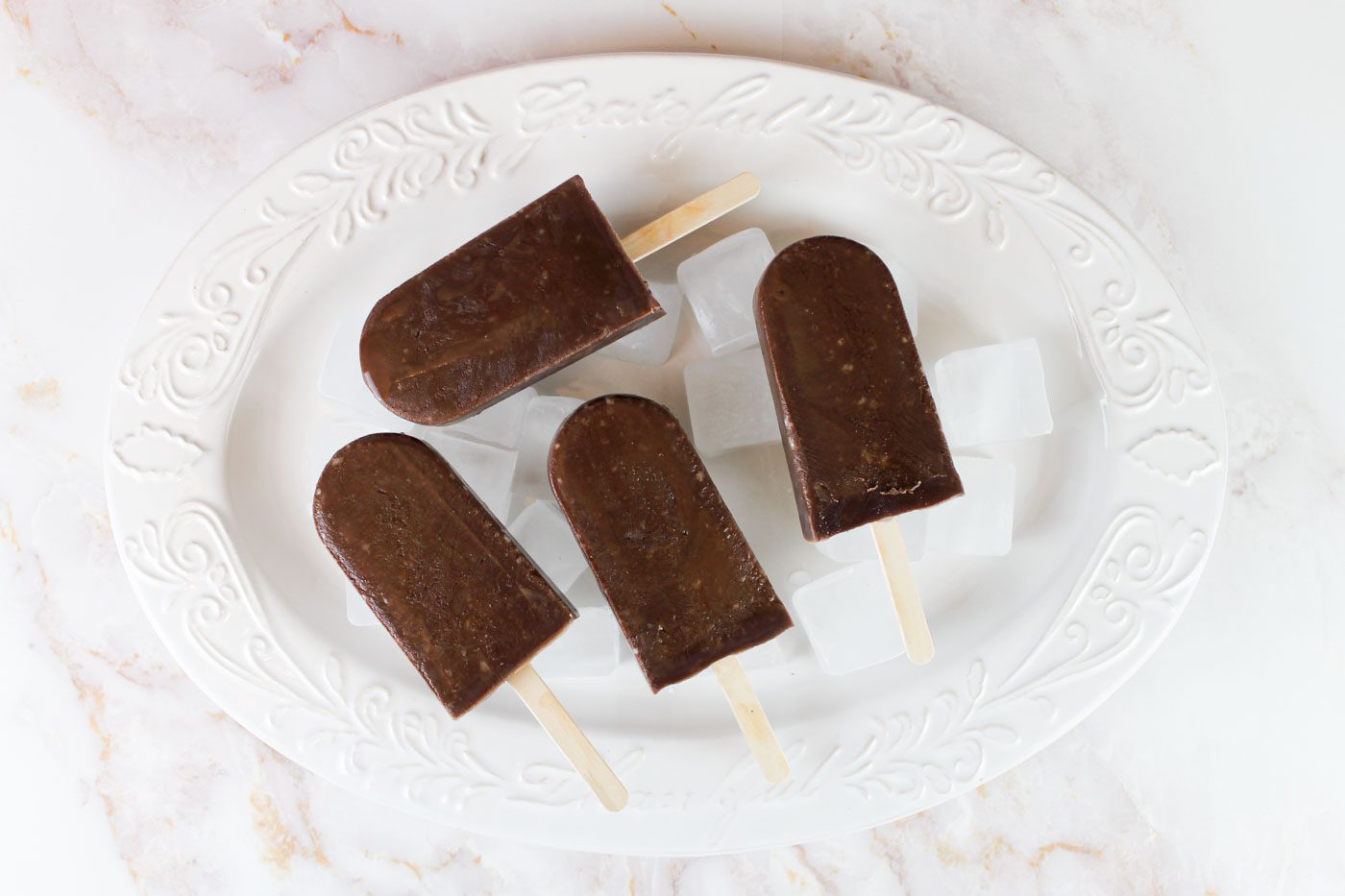 4 chocolate kefir popsicles sit on a large white platter