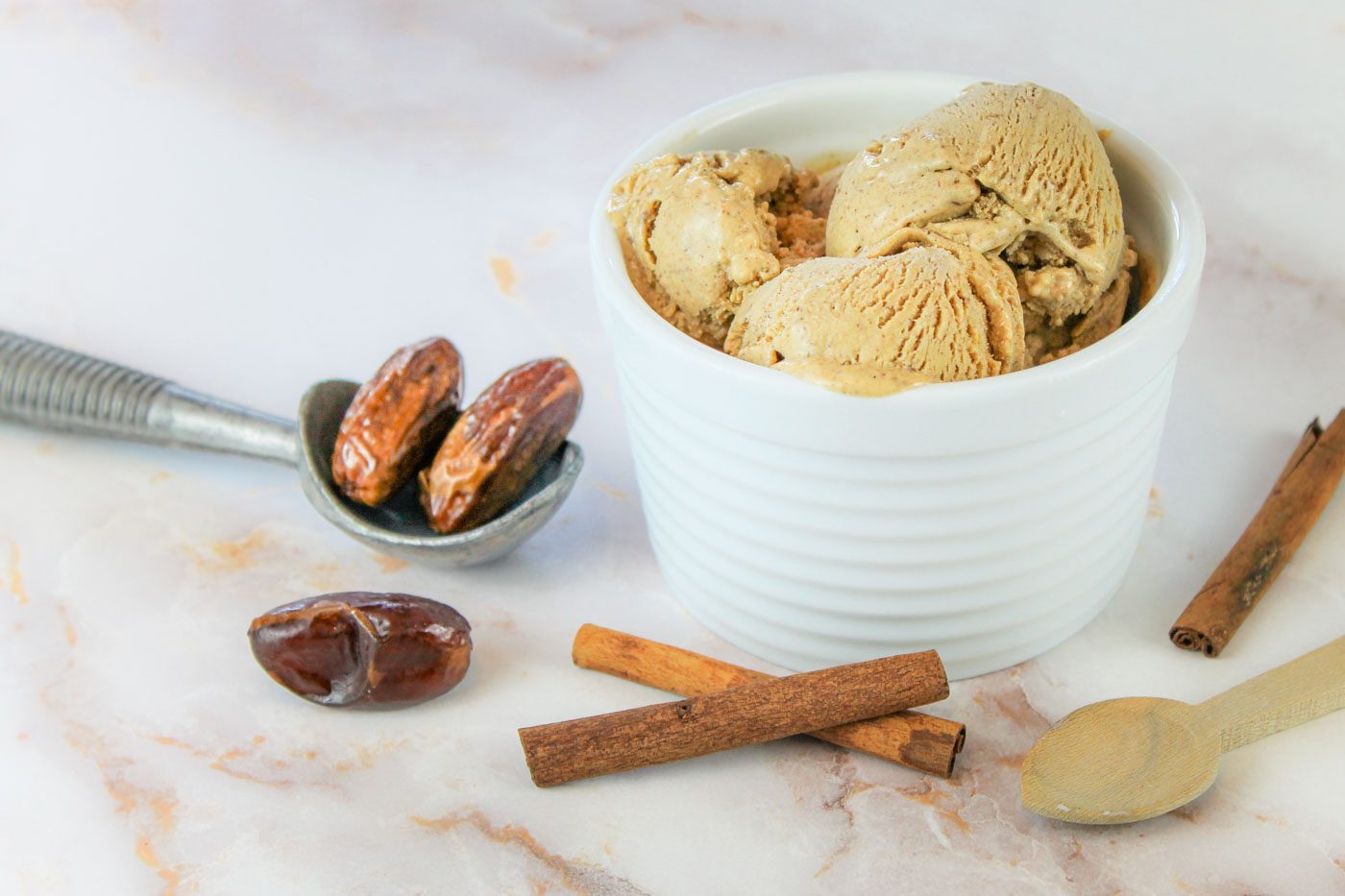 custard bowl of ice cream sits aside spoons, cinnamon sticks and dried dates