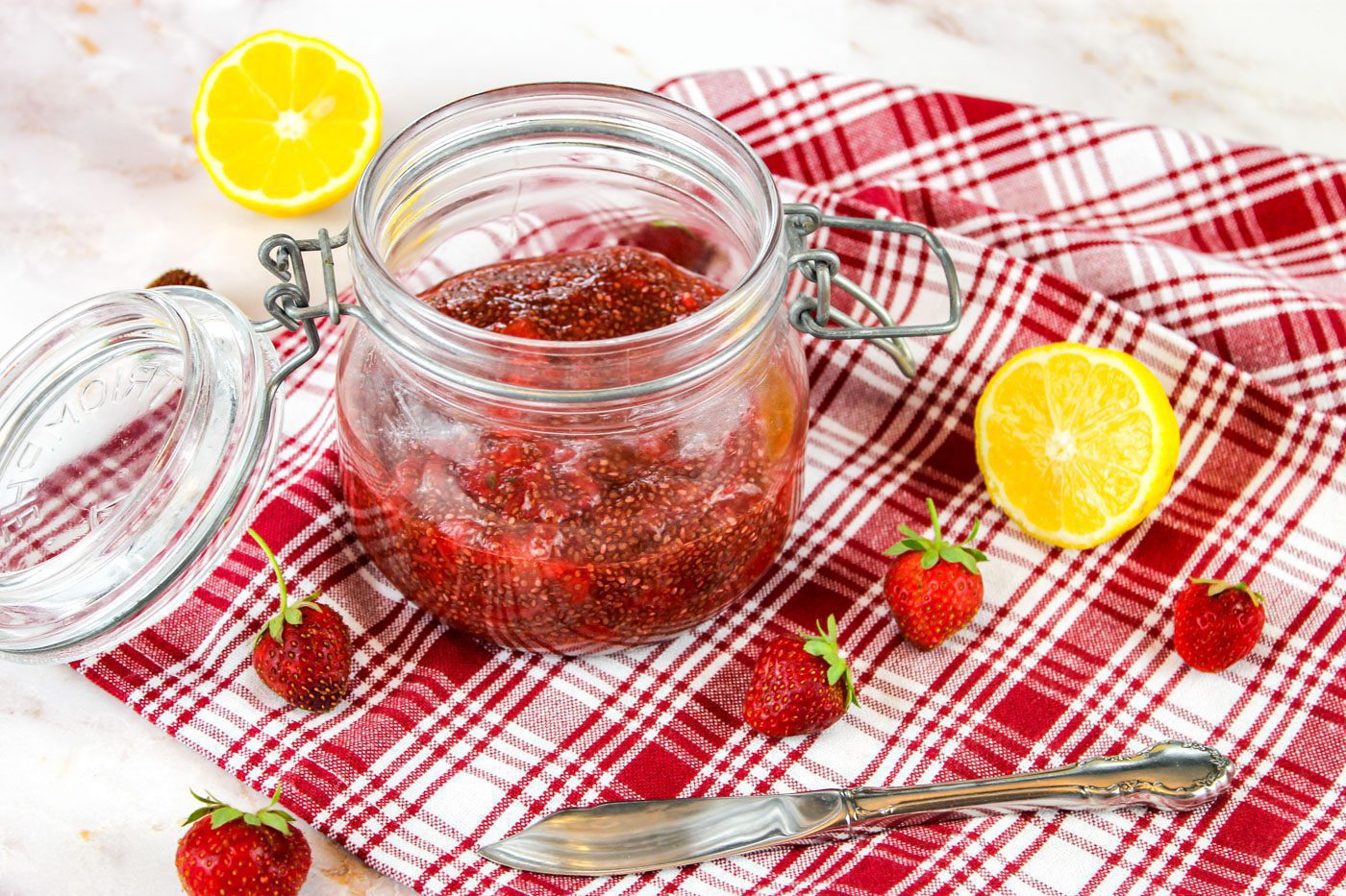 old jar is filled with strawberry jam sitting on top of a plaid kitchen towel