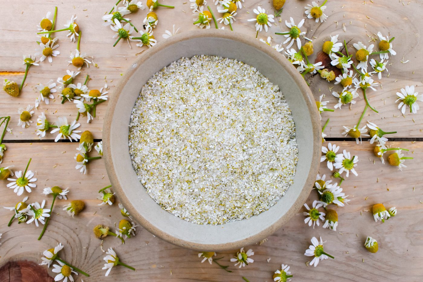 bowl of chamomile bath salt surrounded by scattered flowers