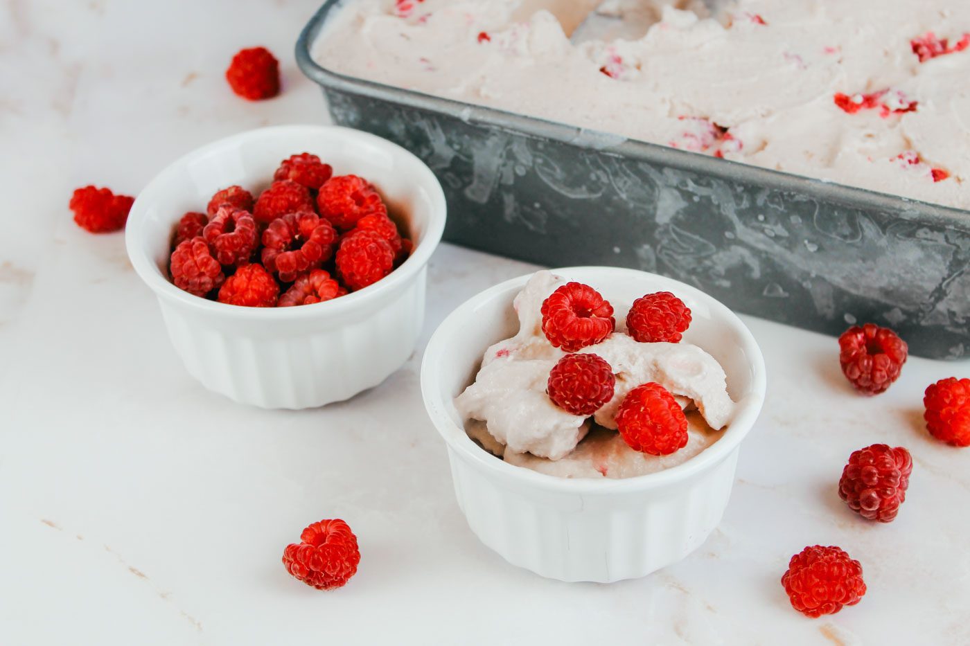 two custard bowls filled with ice cream and fresh raspberries