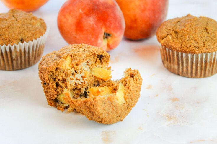 muffin cut in half surrounded by fresh peaches and muffins