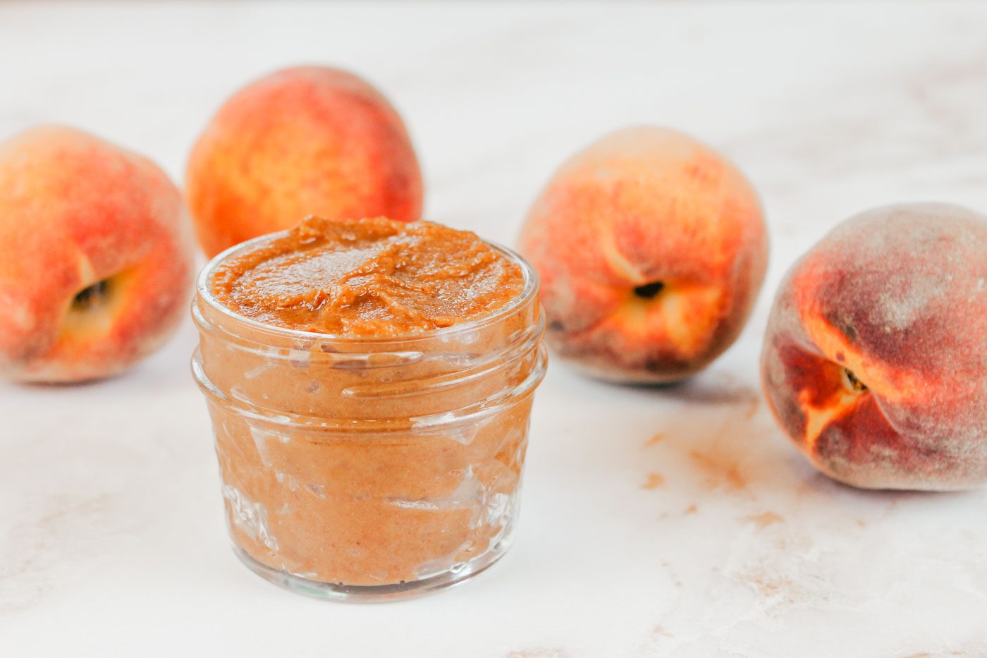 glass jar of peach butter with whole peaches in the background