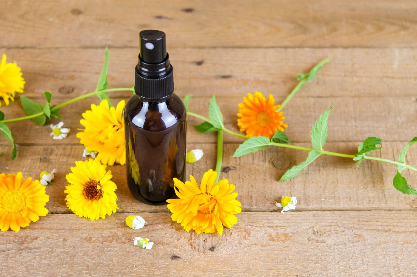 small spray bottle set on a wooden board surrounded by calendula and chamomile