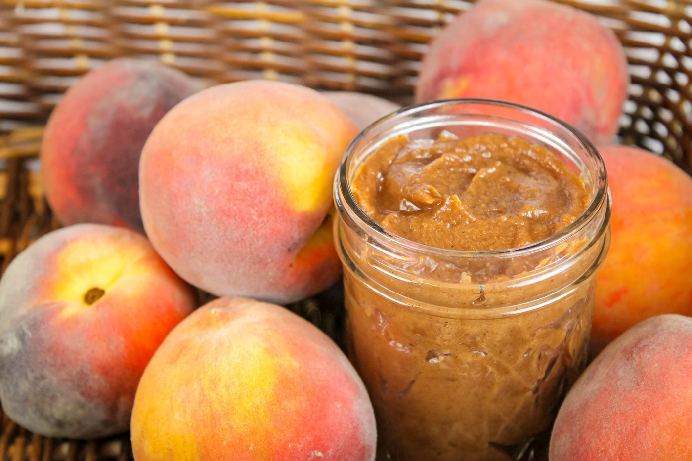 basket full of fresh peaches and jar of peach butter