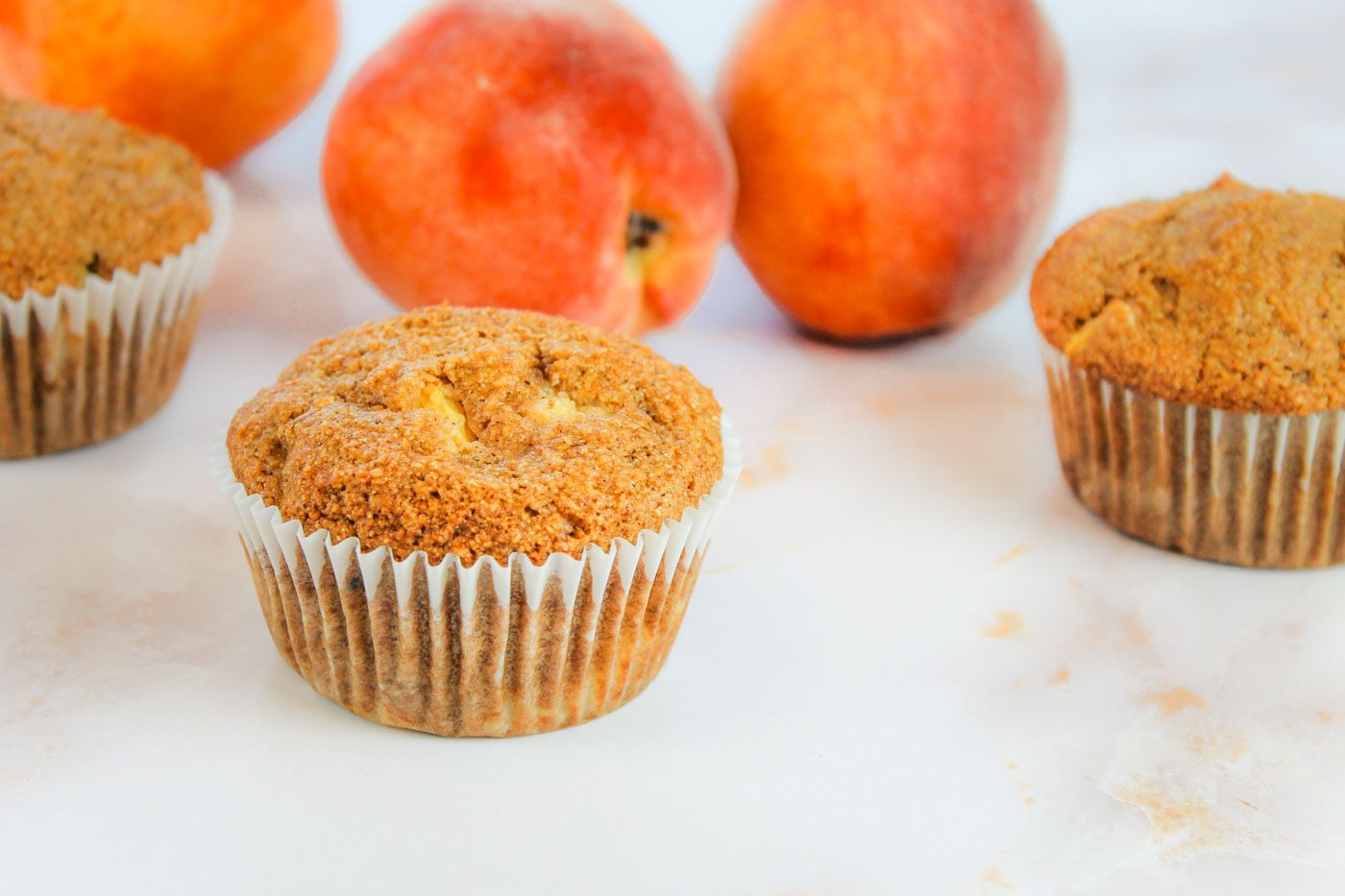 3 peach muffins sit on a marble countertop