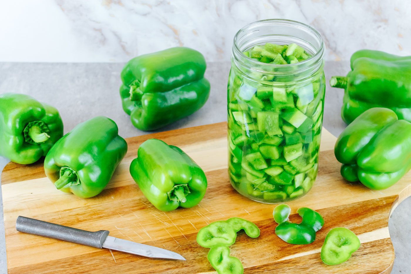 cutting board with green peppers scattered across, jar full of diced peppers sits on the right
