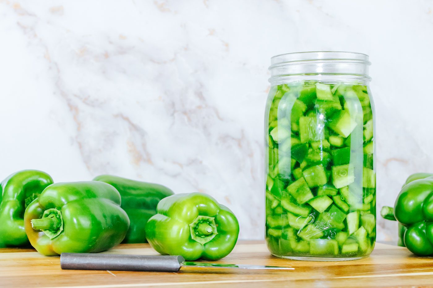 a pile of green bell peppers sits next to a mason jar full of fermented peppers