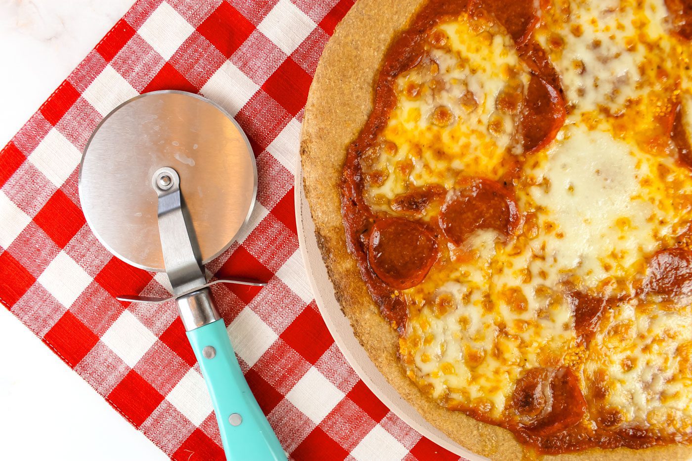 fresh baked pepperoni pizza sits next to a pizza cutter with a teal colored handle