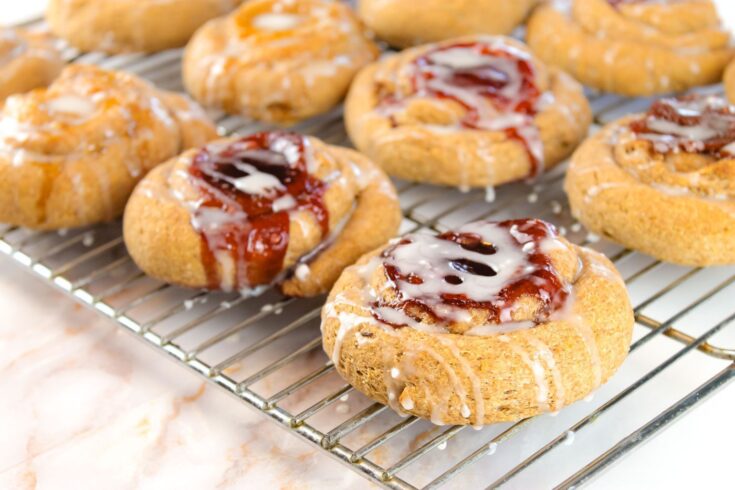 multiple homemade danishes sit on a cooling rack with a white vanilla glaze dripping off the sides of each pastry