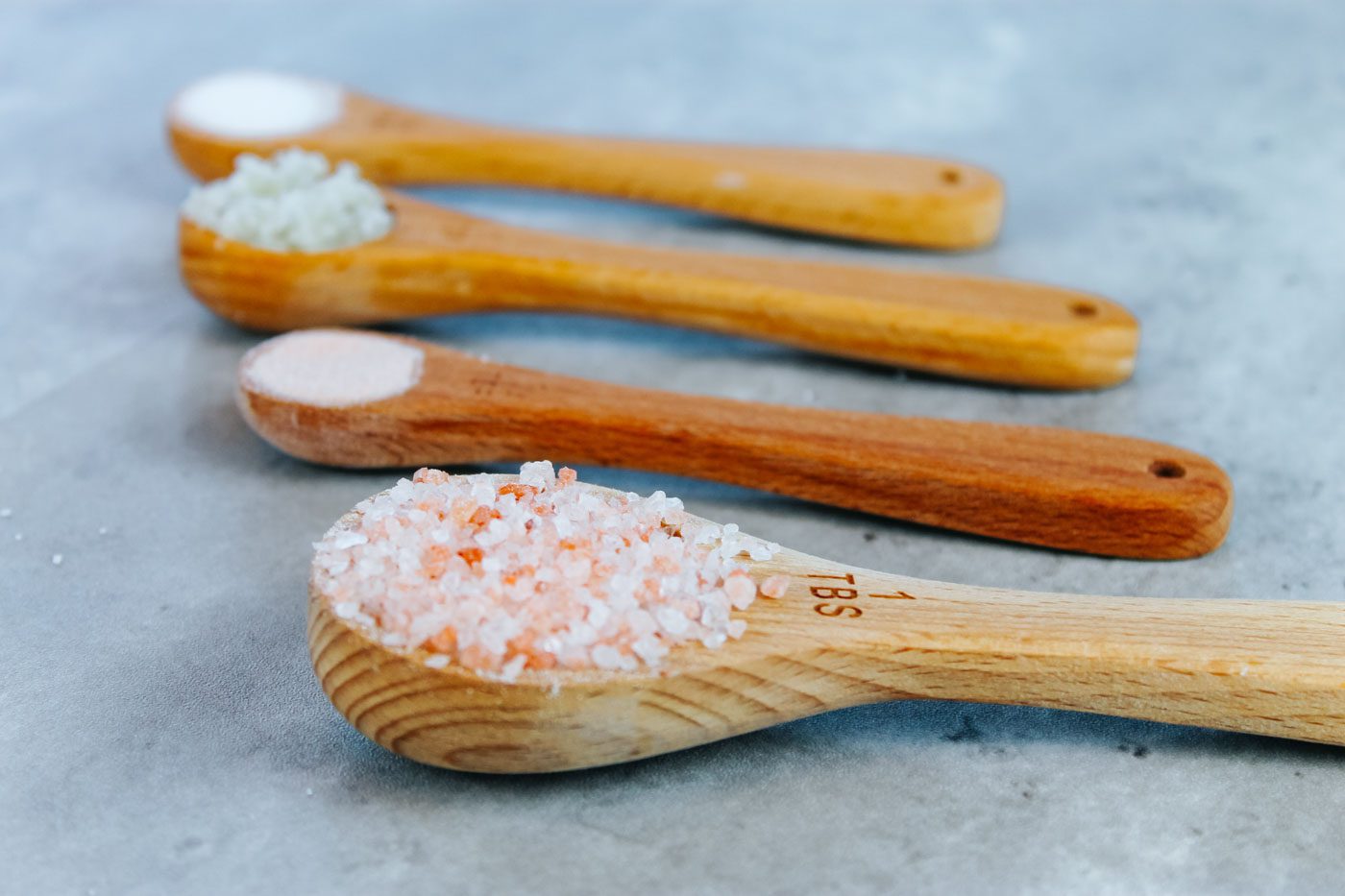 four measuring spoons full of different types of salts
