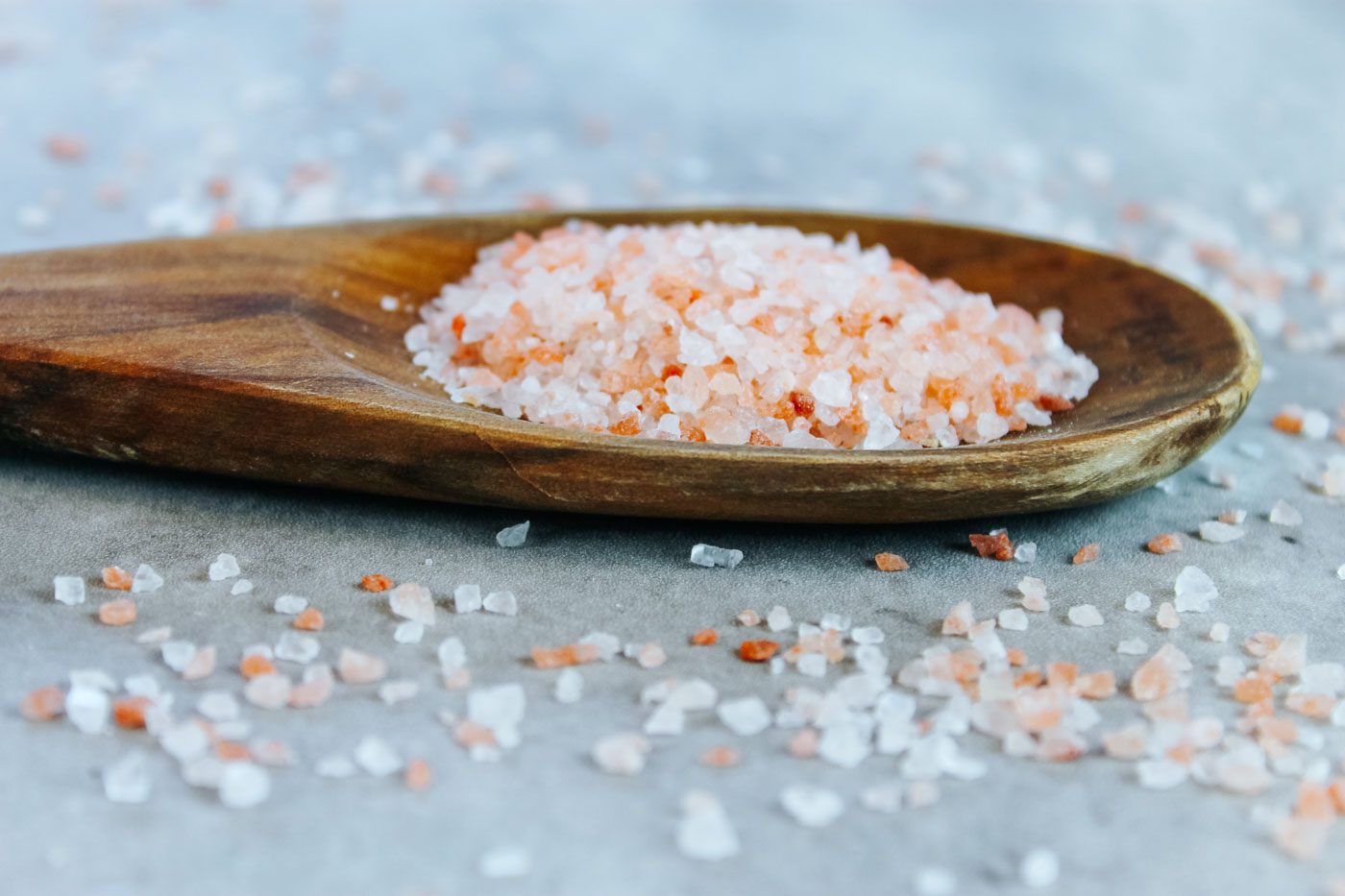 close up of a wooden spoon full of coarse pink himalayan salt for fermenting