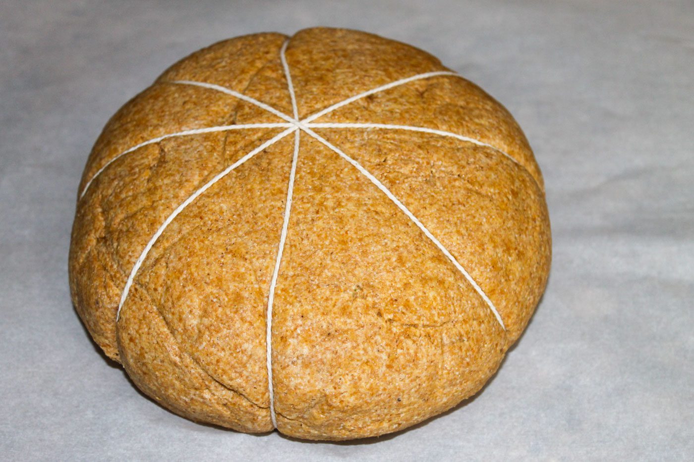 loaf of dough tied with eight pieces of string to make a pumpkin shaped bread