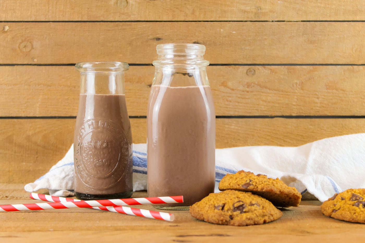 two bottles sit beside a stack of chocolate cookies and a pie of red and white striped straws