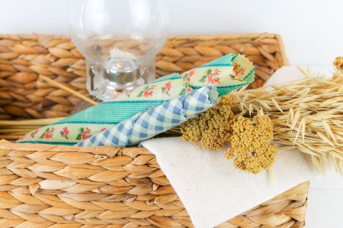 weaved basket full of beeswax wraps, dried natural, a piece of linen and an oil lamp