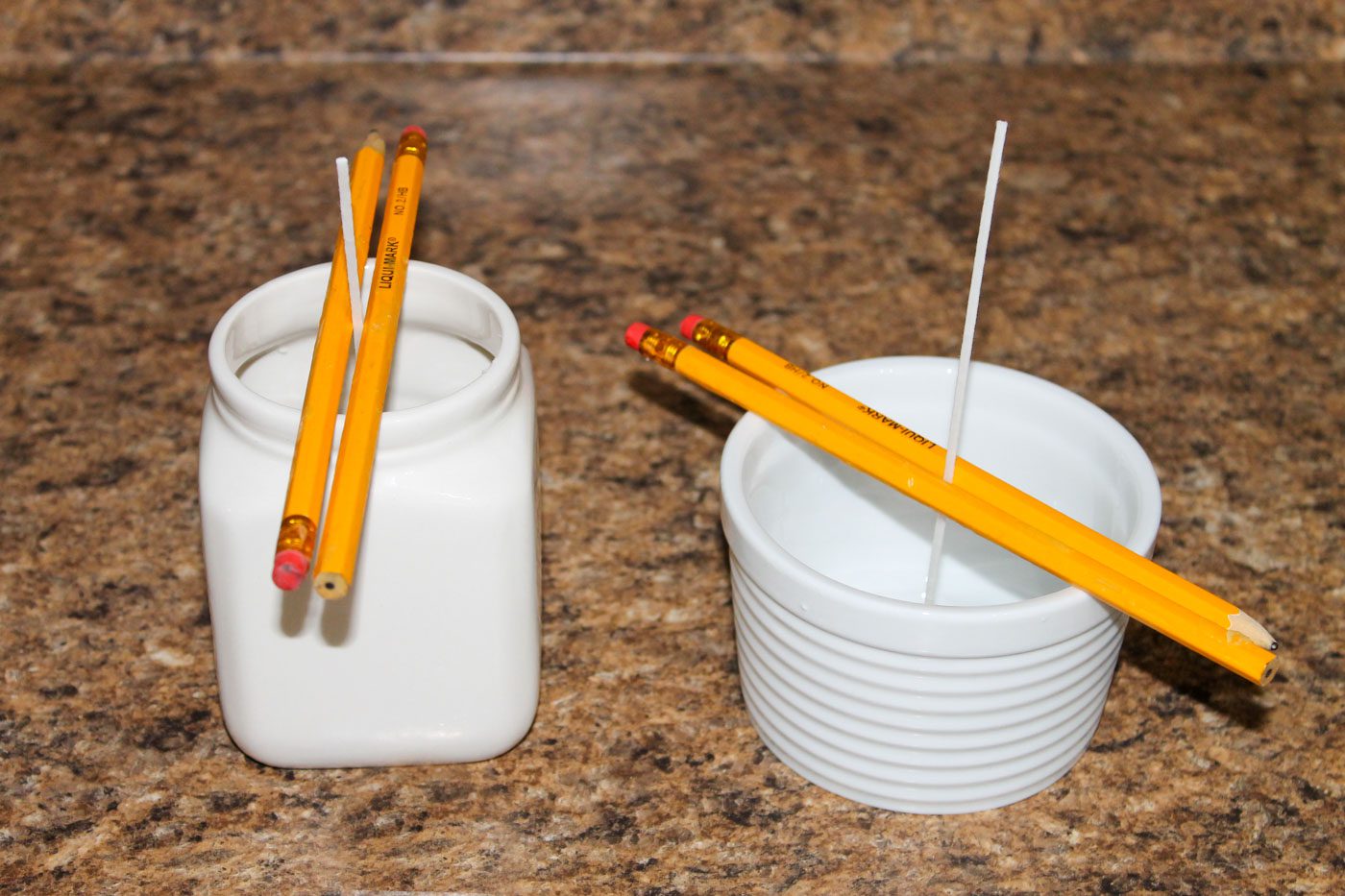 two white containers with pencils on top to stabilize candle wicks in the center