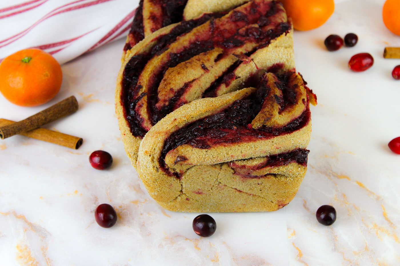 side view of cranberry bread with fresh cranberries, oranges and cinnamon sticks scattered about