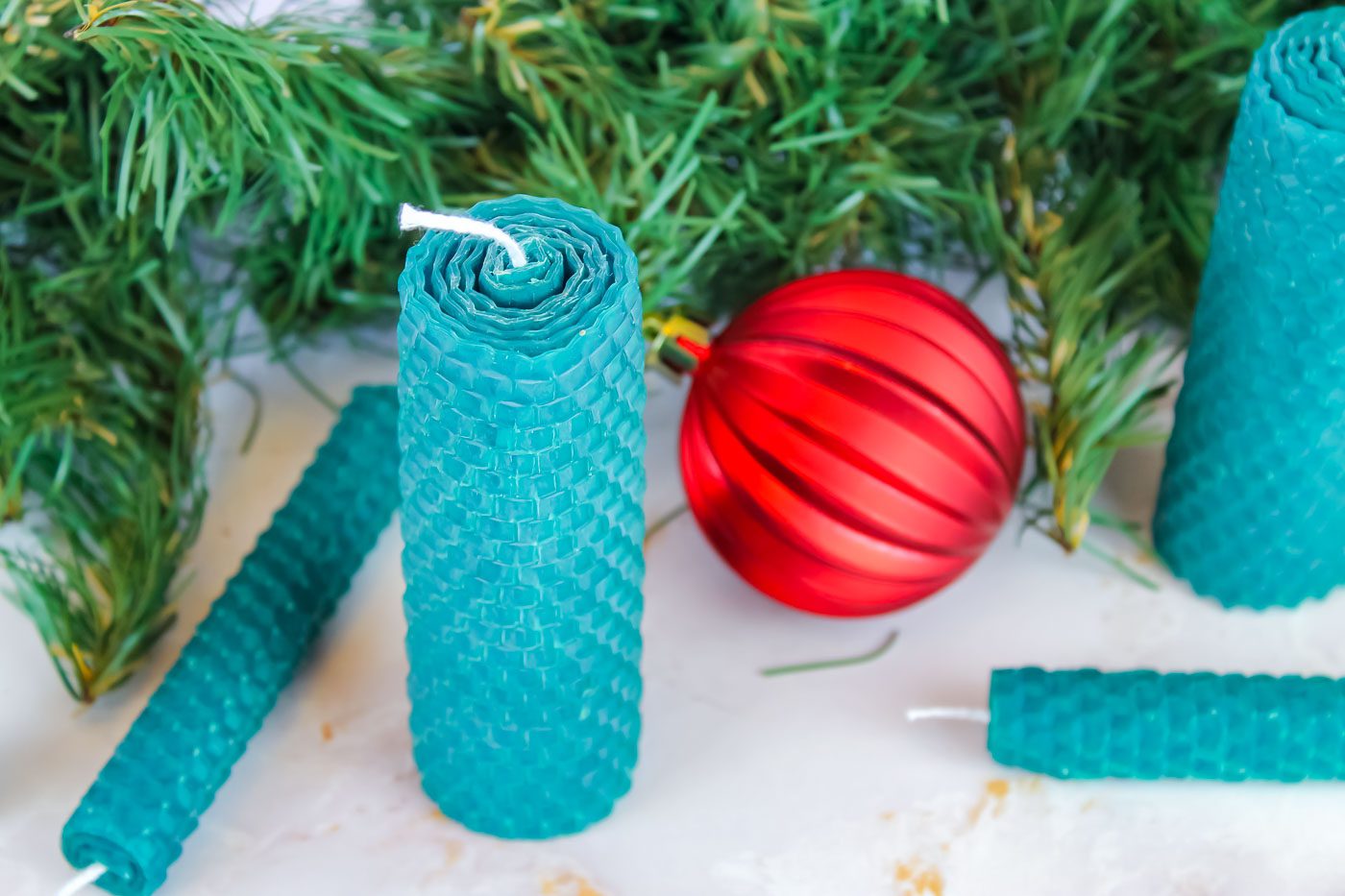 green rolled beeswax candles sitting in front of a red Christmas ornament and some pine greenery