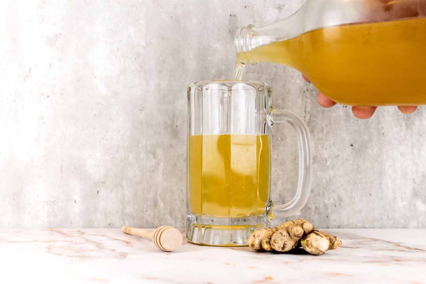 bottle of fermented ginger ale slowing pouring into a glass mug