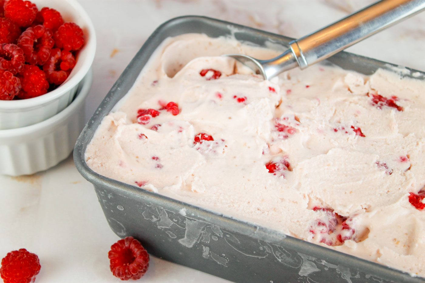 metal tin filled with ice cream surrounded by fresh raspberries